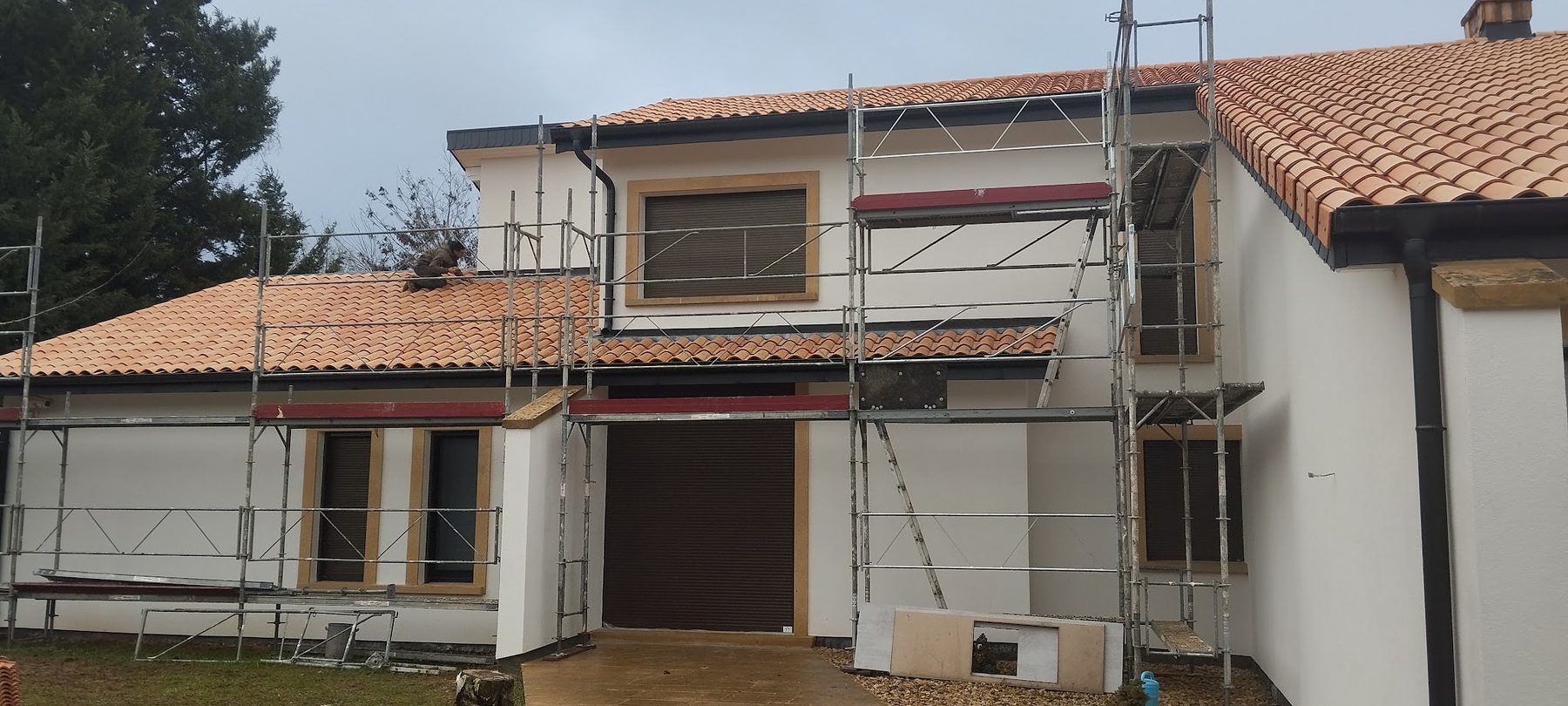Maison sous échafaudage, toiture neuve en tuiles canal orangées, couvreur au travail sur le pan bas