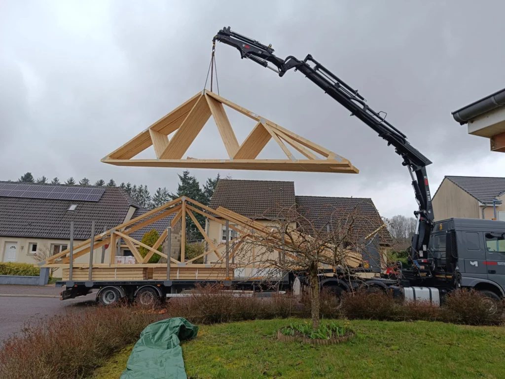 Ferme en bois suspendue au bras d'un camion-grue devant des maisons