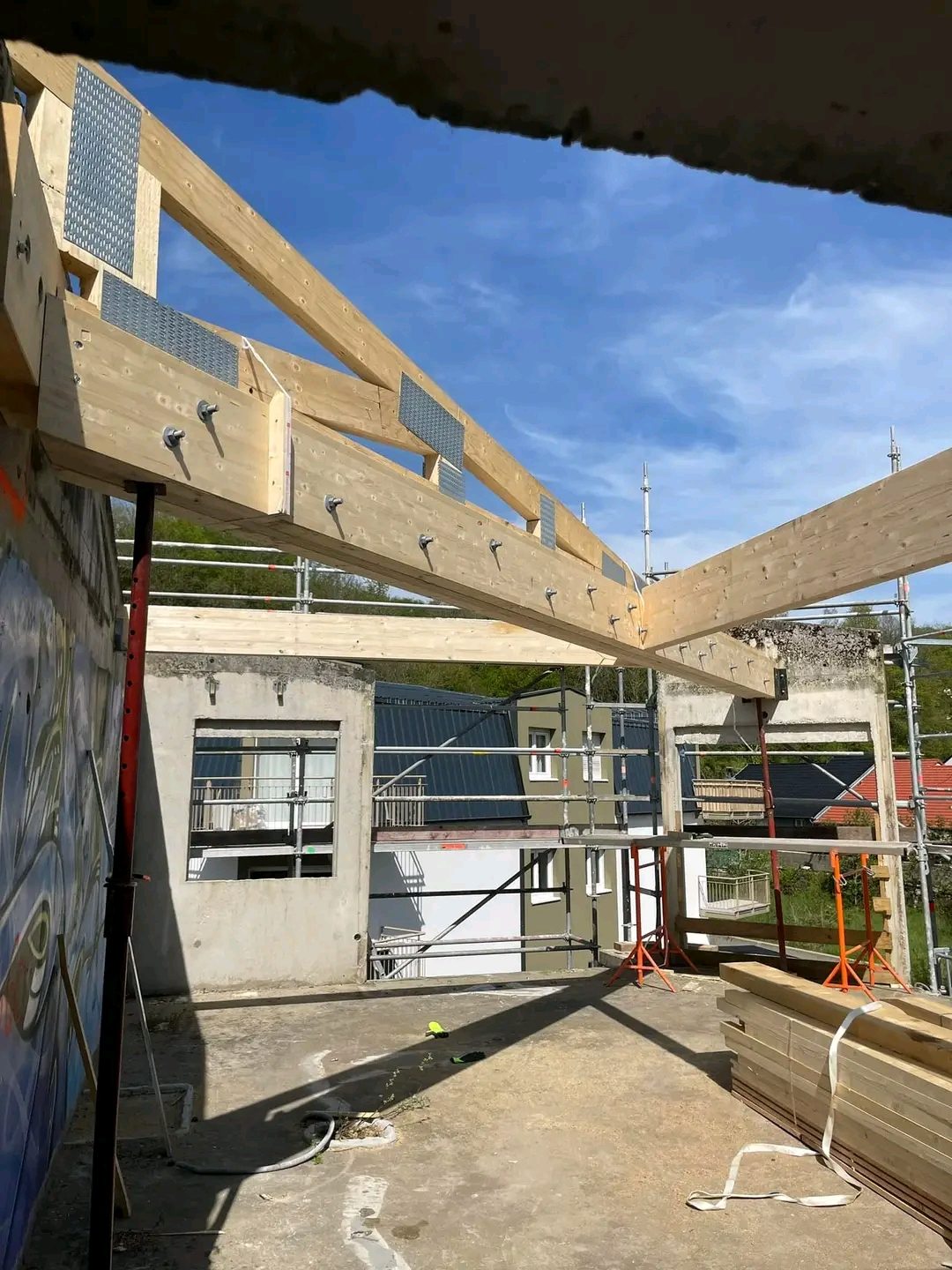 Charpente neuve en bois posée sur des murs en béton, sous un ciel bleu